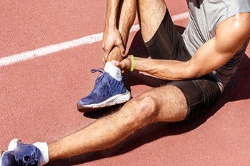 Man holding onto sore ankle - sports medicine